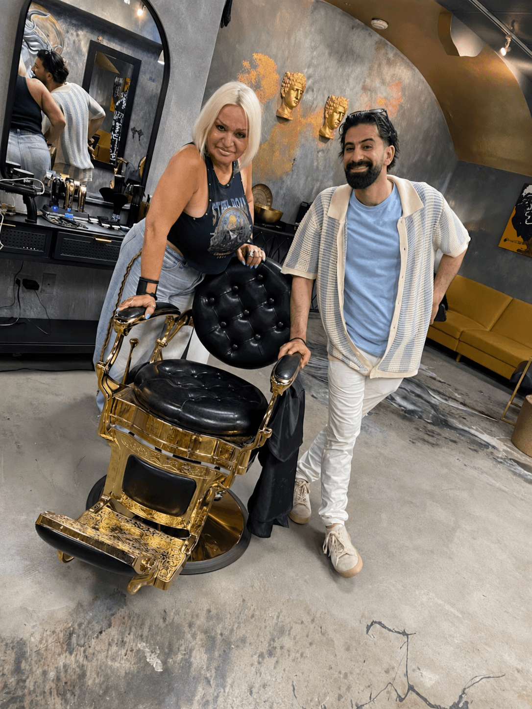 Lui and Danuta standing by a gold barber chair in the shop